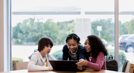 three students sitting around a laptop screen 